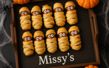 Mummy-wrapped sausages displayed on a custom serving tray with Halloween decor